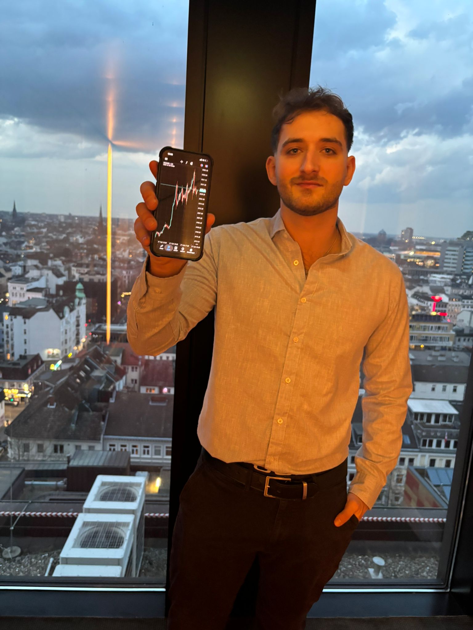 Peer, Gründer von PNTRADES, mit einem Trading-Chart auf dem Smartphone vor der Stadtskyline